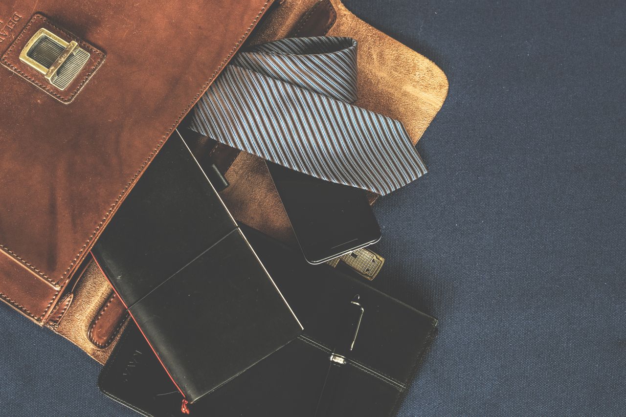 Services-01 Flat lay of men's leather bag with accessories like a tie, notebook, and phone. Ideal for business themes.