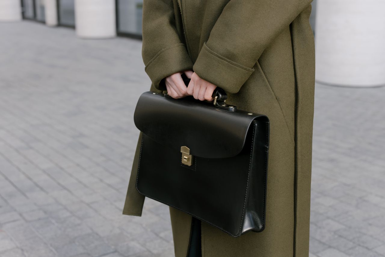 Services-03 Close-up of a woman in a coat holding a black briefcase on a paved street.