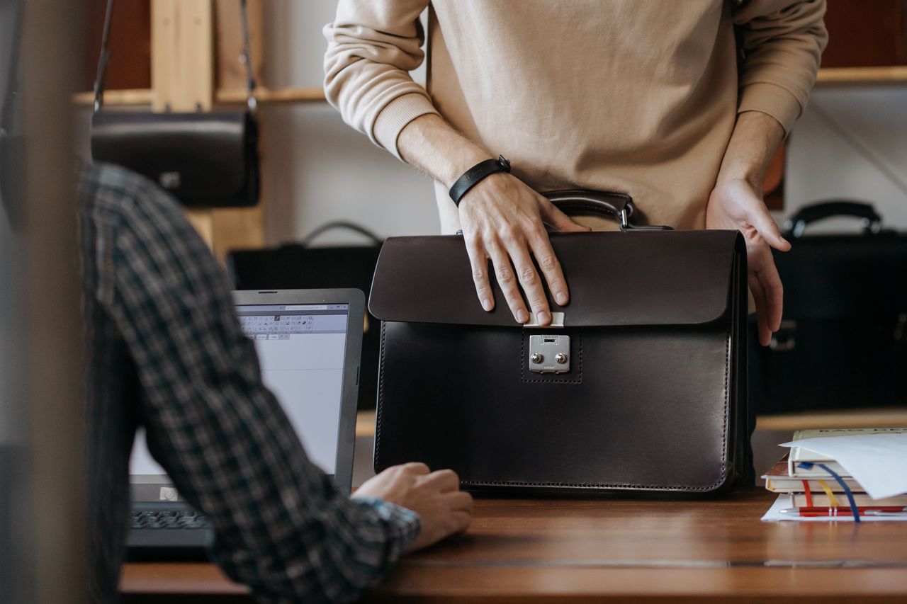Services-02 Close-up of two professionals handling a leather briefcase in an office setting.